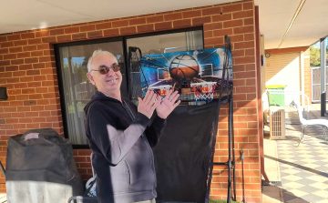 Older male smiling, standing in front of a small basketball hoop structure.