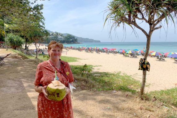 Woman holding a fresh coconut drink. She is standing in front of a tropical beach.